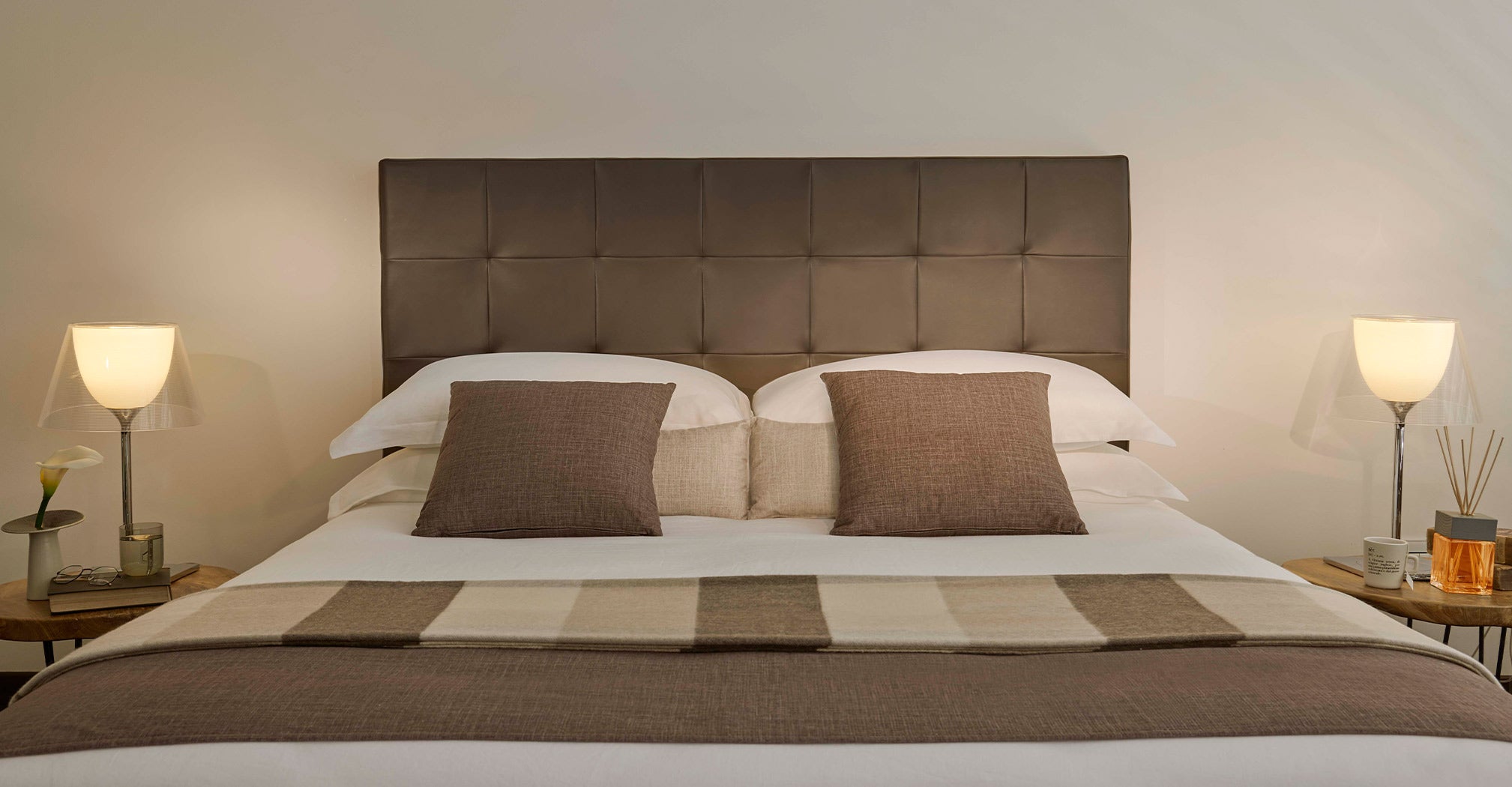 A cozy bed with a headboard flanked by two stylish lamps, set in a cruise-themed room for a night at sea.